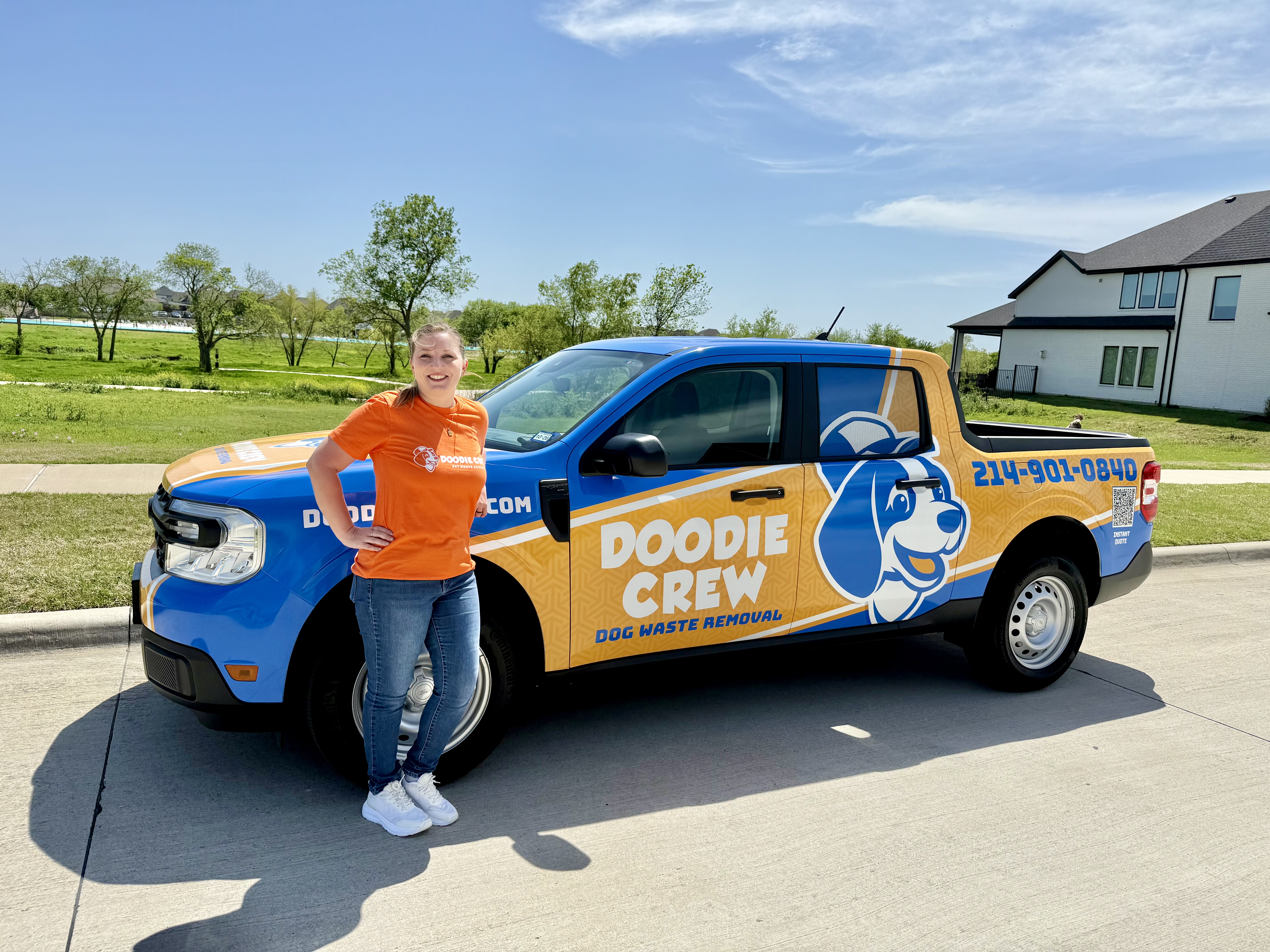 Doodie Crew team member in orange shirt standing confidently in front of the branded service truck ready for a dog waste removal visit in Prosper, TX