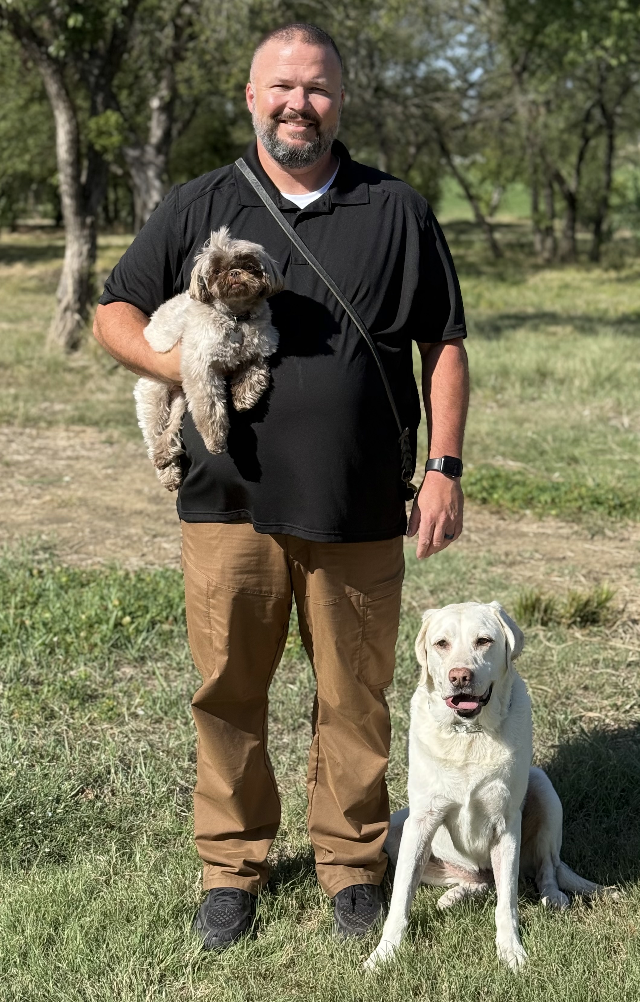 Ryan White, founder of Doodie Crew and certified dog trainer, holding a small dog with a white Labrador by his side in Prosper, TX